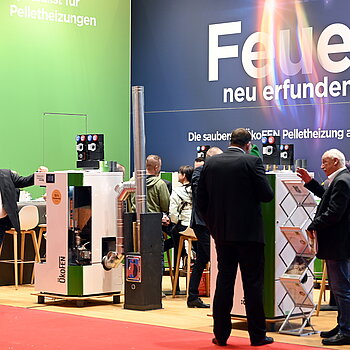 Der Messestand zeigt Pelletheizungen von ÖkoFEN, umgeben von Fachleuten und Besuchern, die sich über nachhaltige Heizsysteme informieren.