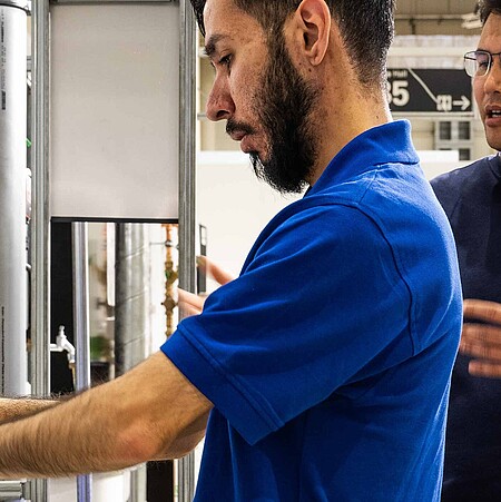 Ein Mann testet eine Apparatur im TechnikPark. Eine weitere Person steht erklärend hinter ihm.