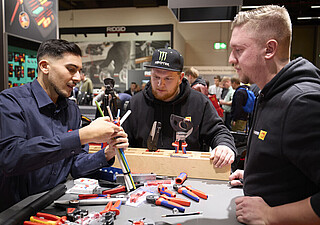 Drei Männer stehen an einem Werktisch und arbeiten mit Kabeln.